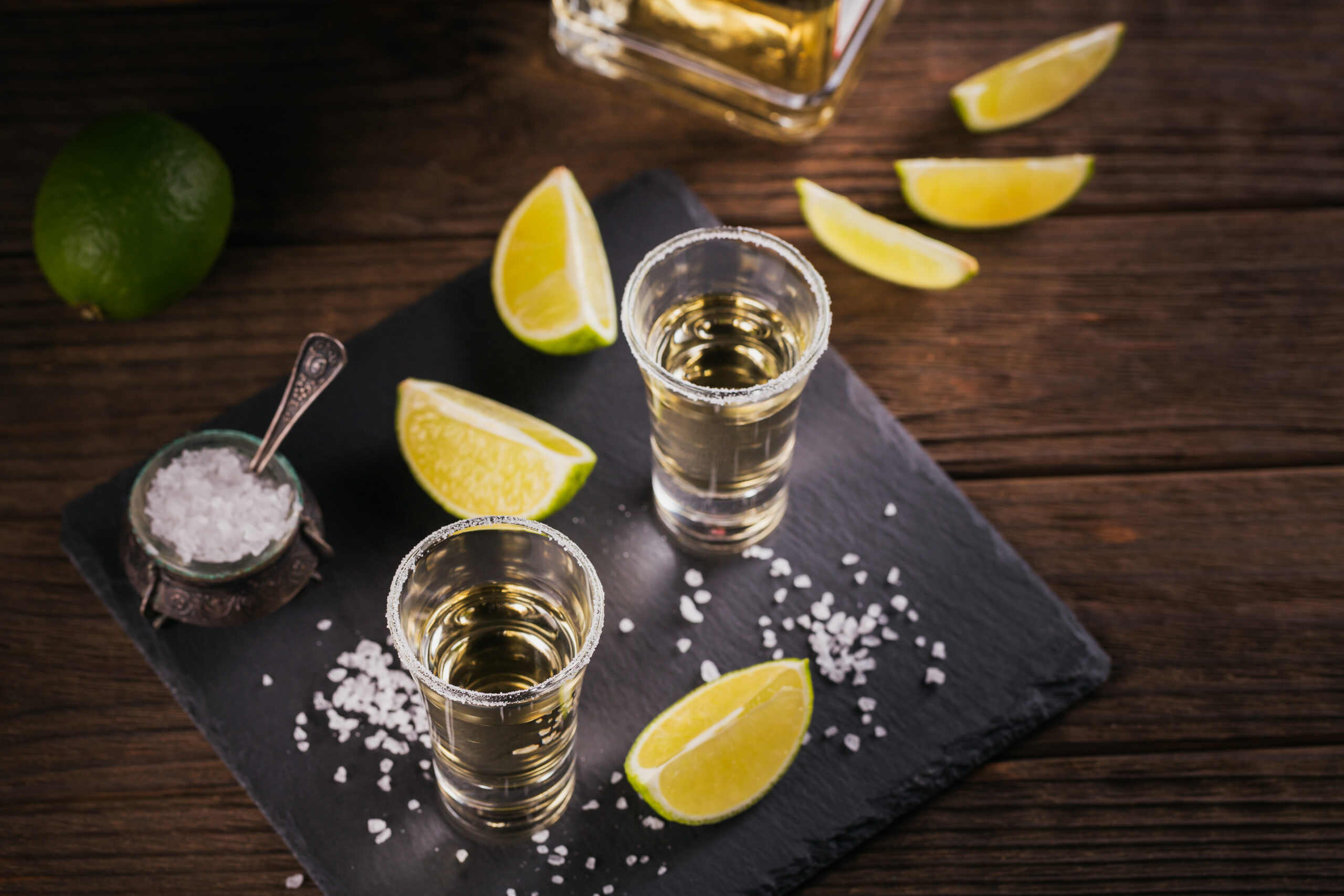 Gold tequila shot with lime and sea salt on black table. Top view